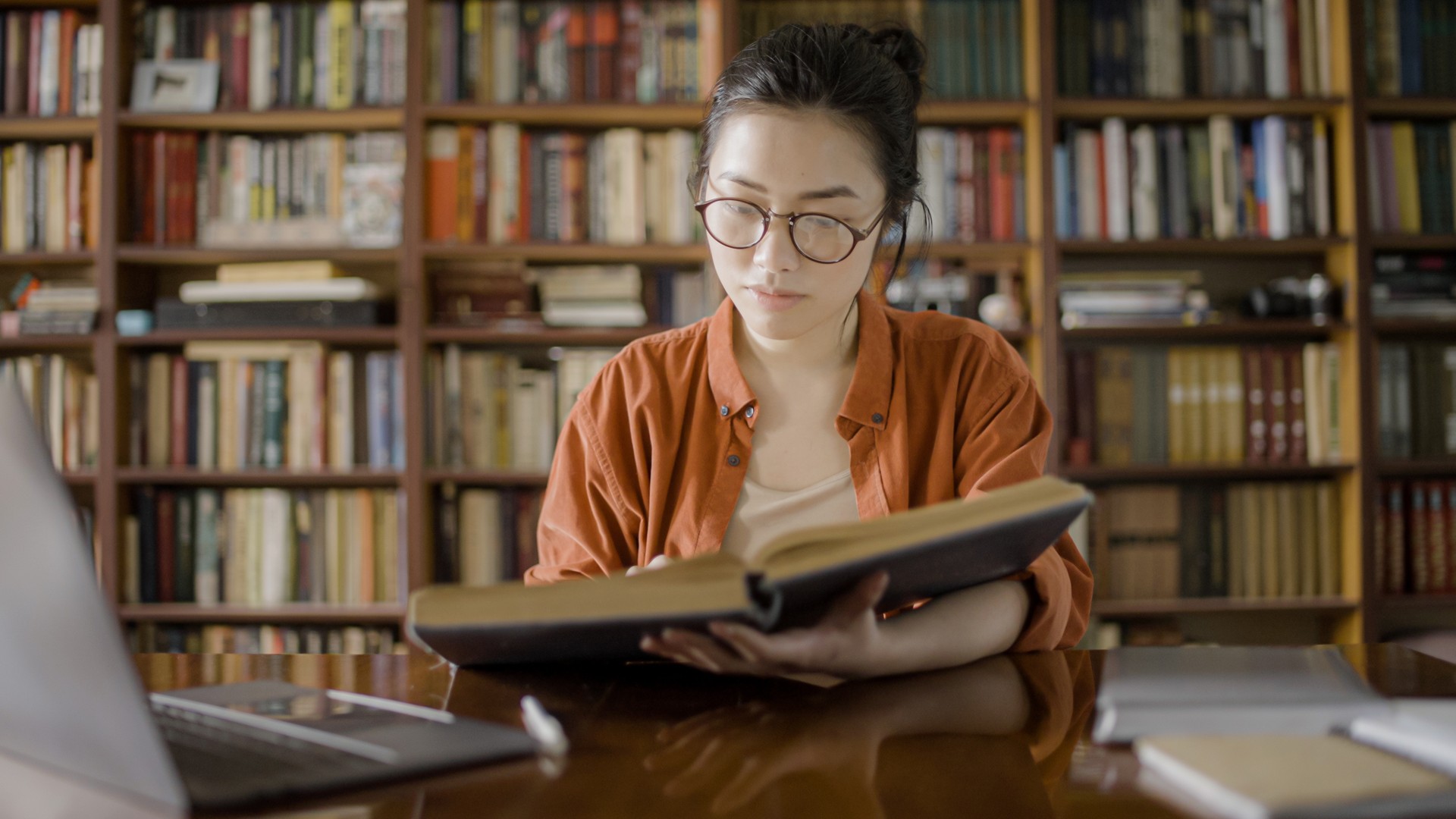 Young beautiful woman reading large book in a library, doing research for work project